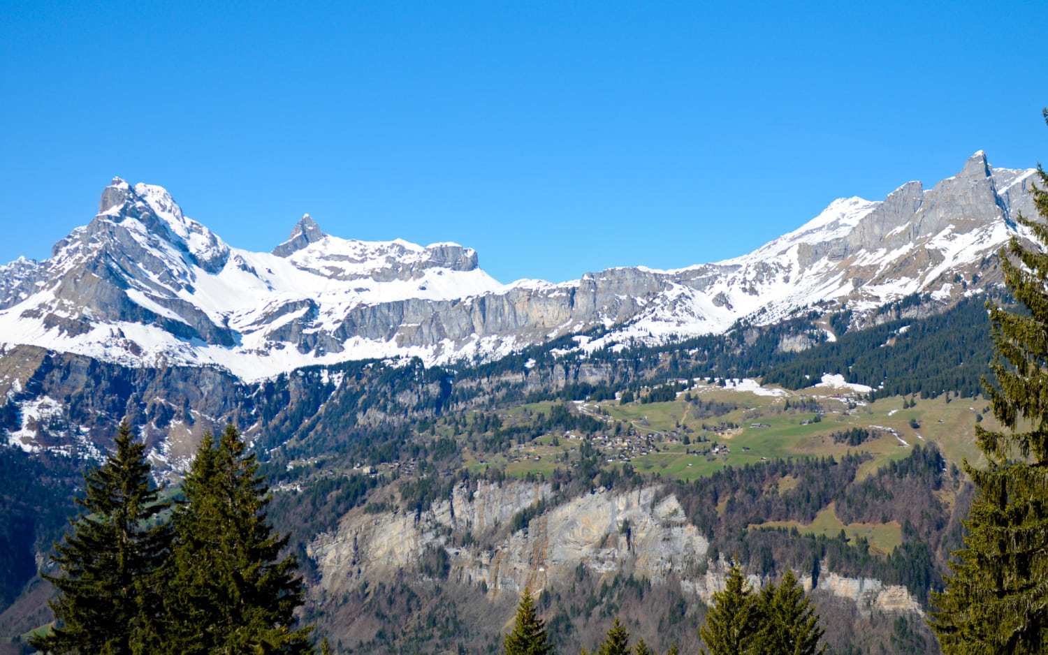 Snow-capped jagged peaks above a green alpine valley with a small mountain village, near Braunwald