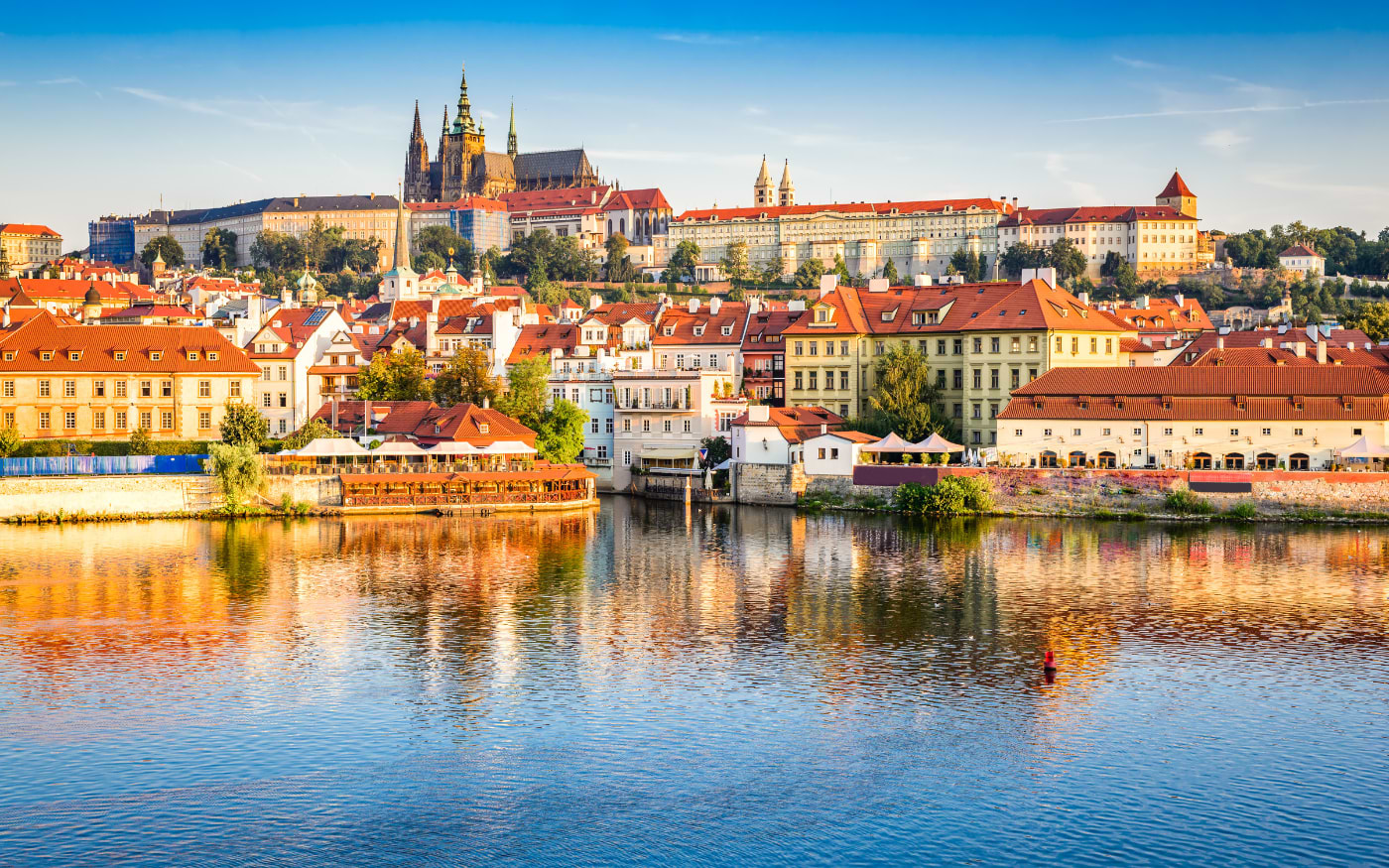 Prague Castle and St Vitus Cathedral above the red roofs of MalĆ” Strana, reflected in the Vltava River at golden hour