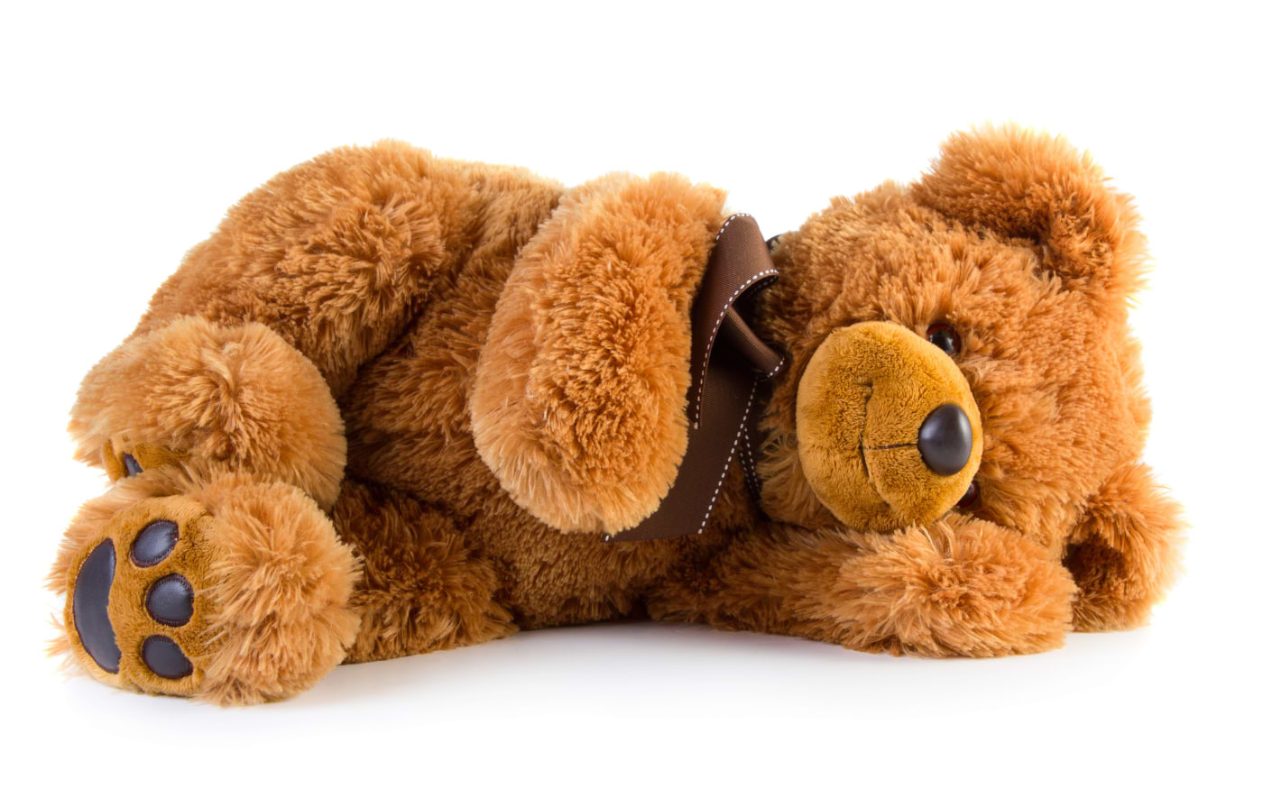 Brown plush teddy bear lying down with a ribbon bow around its neck