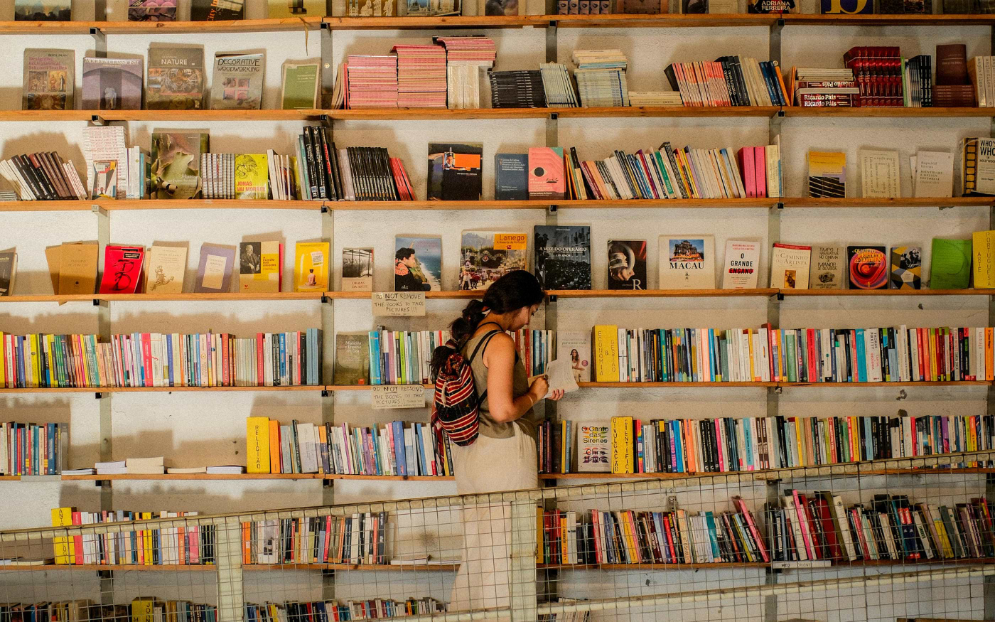 Woman browsing colorful bookshelves in a traditional Portuguese bookshop filled with local literature and titles.
