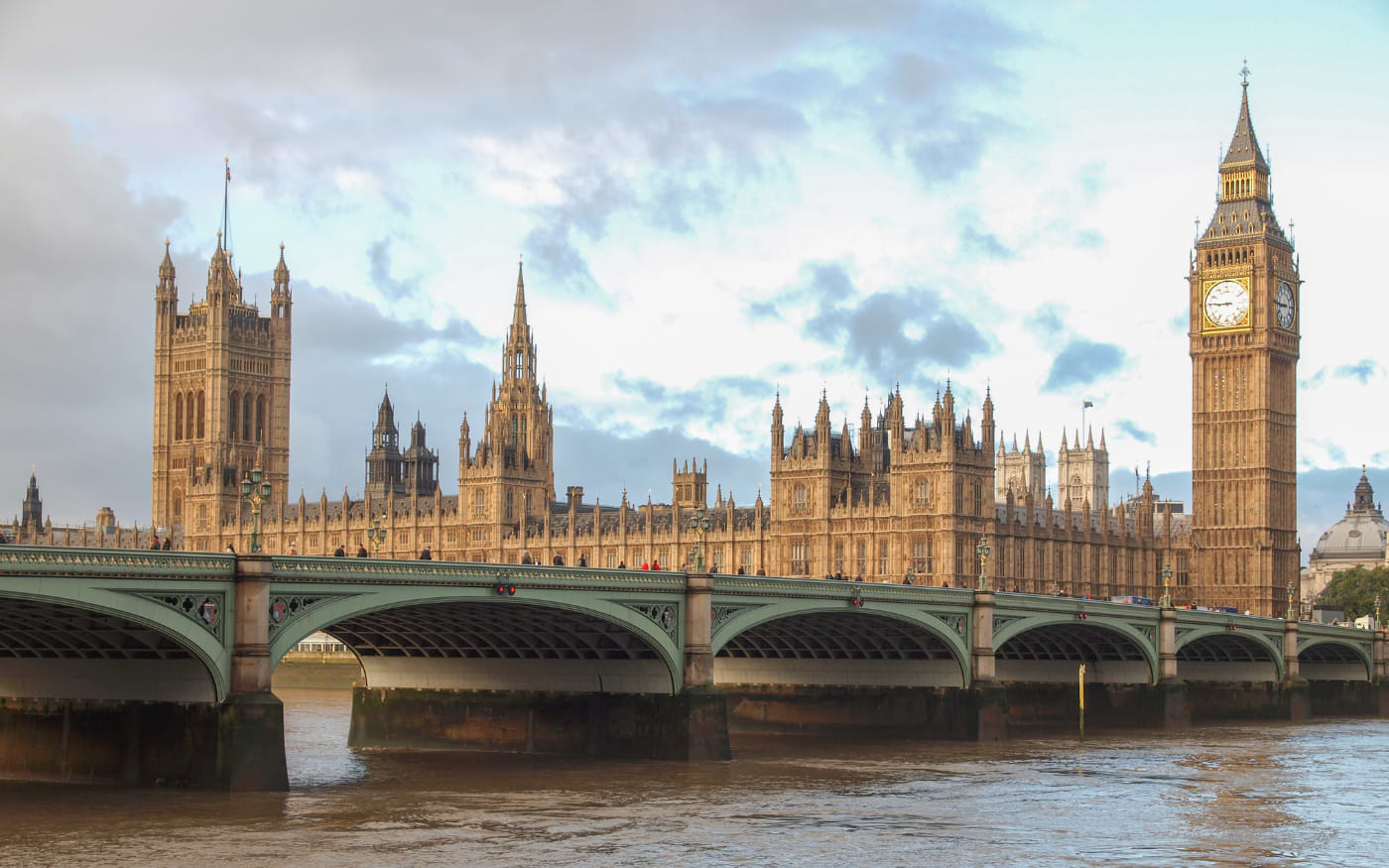 Houses of Parliament and Big Ben behind the green arches of Westminster Bridge on the River Thames under a cloudy sky