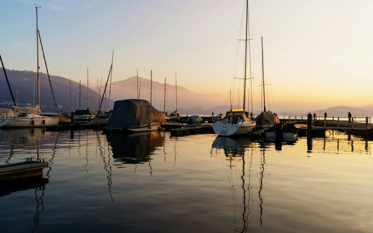 Sailboats moored in a calm harbour at sunset with mountains behind, near the Zugerberg viewpoint