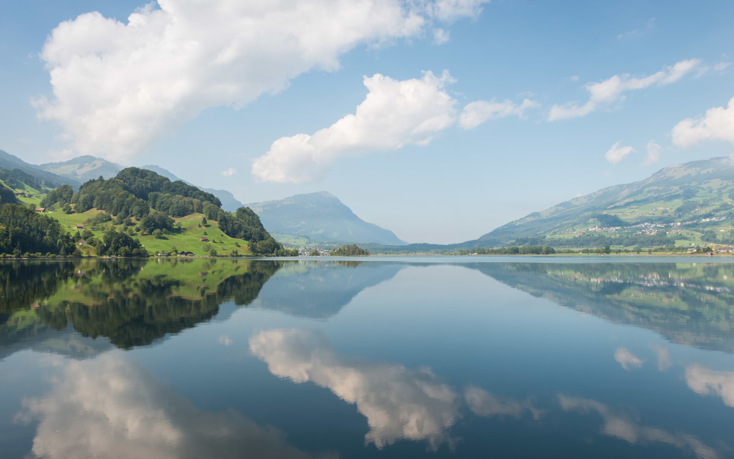 Still lake mirroring green hills and clouds, similar to the Lake Lauerz view from Sattel-Hochstuckli