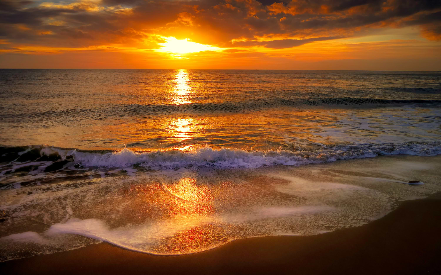 A golden sun sets over the Mediterranean Sea near Palma de Mallorca, its warm light reflecting across gentle waves rolling onto the shore.
