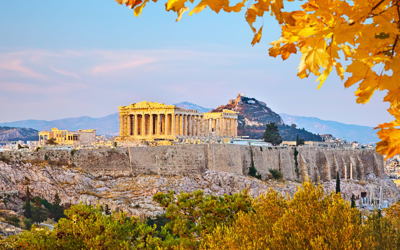 The Parthenon and Erechtheion on the Acropolis in Athens in soft evening light, Lycabettus Hill behind and autumn leaves