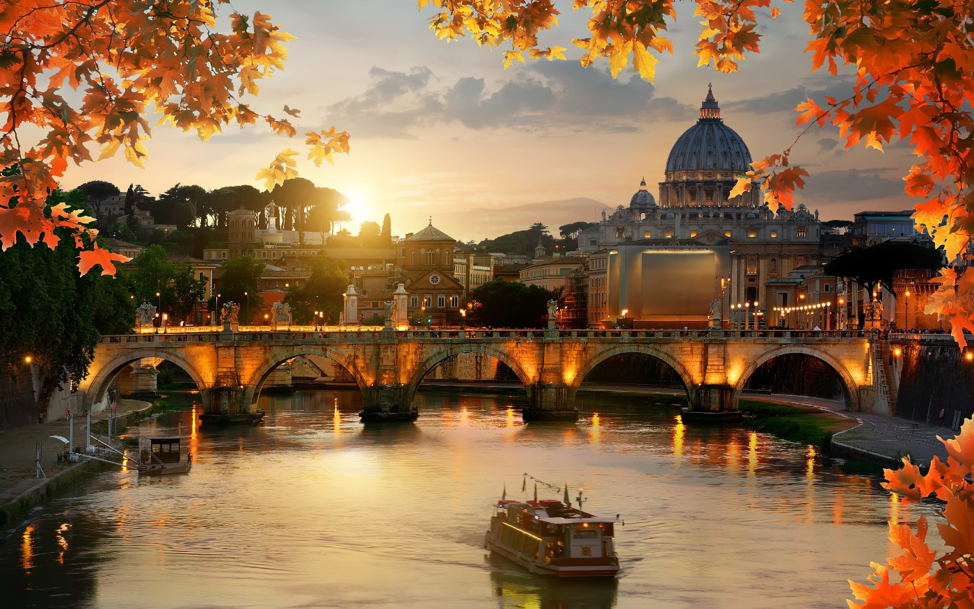 Ponte Sant'Angelo over the Tiber in Rome at sunset with the dome of St Peter's Basilica, framed by orange autumn leaves