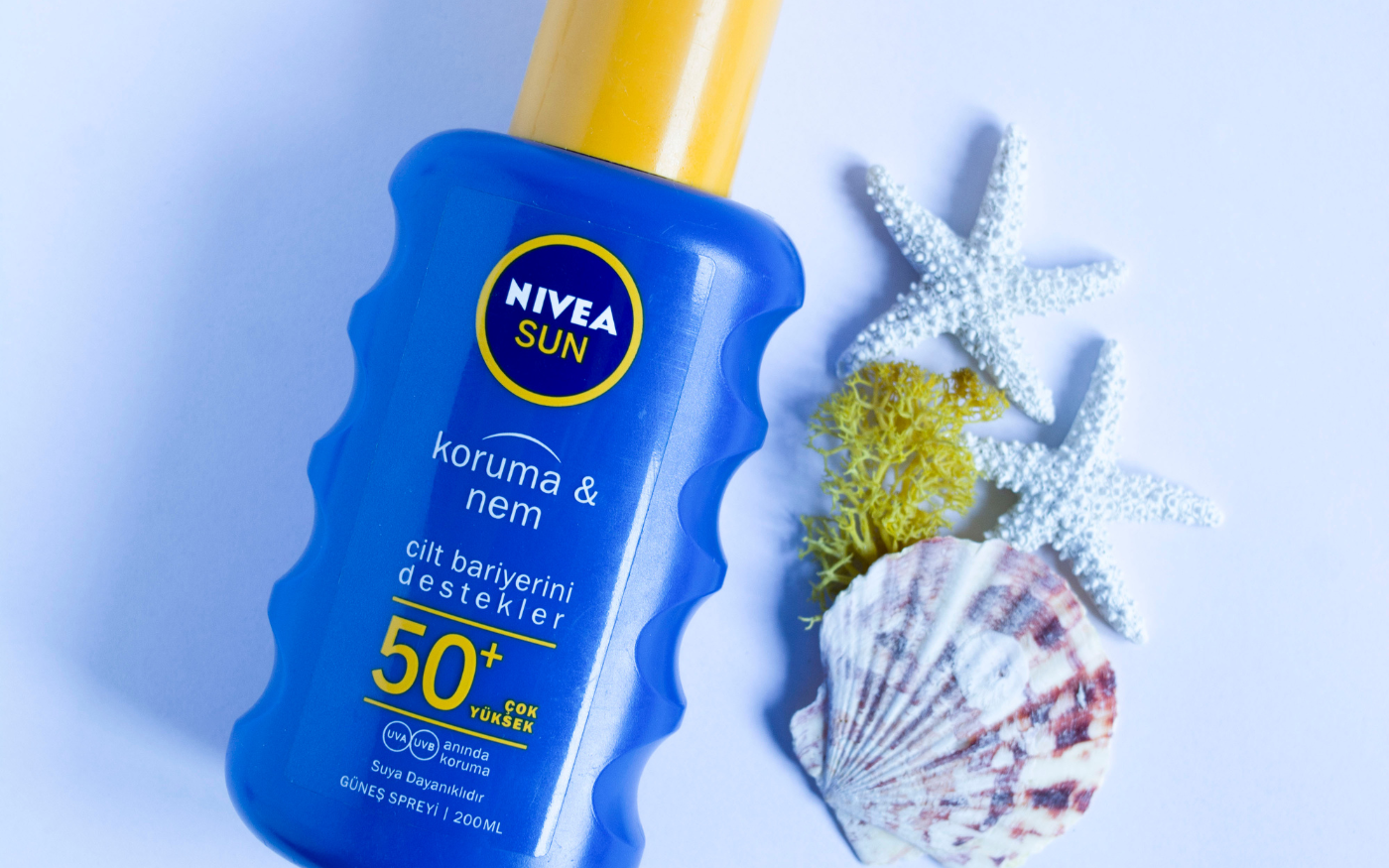 Nivea Sun sunscreen spray bottle beside starfish and a seashell