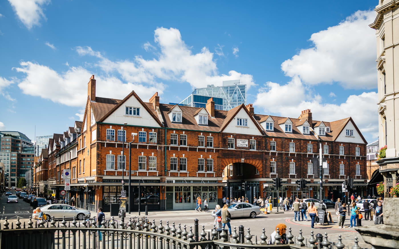 Red-brick Victorian facade of Old Spitalfields Market with white gables and an arched entrance under a blue sky
