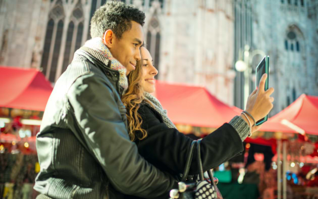 Festively decorated wooden stalls at Milan's Piazza Duomo Christmas Market, with a couple browsing handcrafted ornaments and seasonal treats