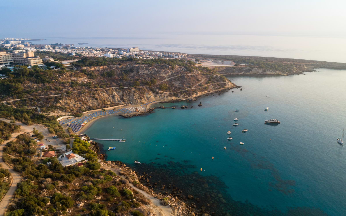 Aerial view of Protaras bay with turquoise water, rocky coastline, and boats floating in the sea, Cyprus
