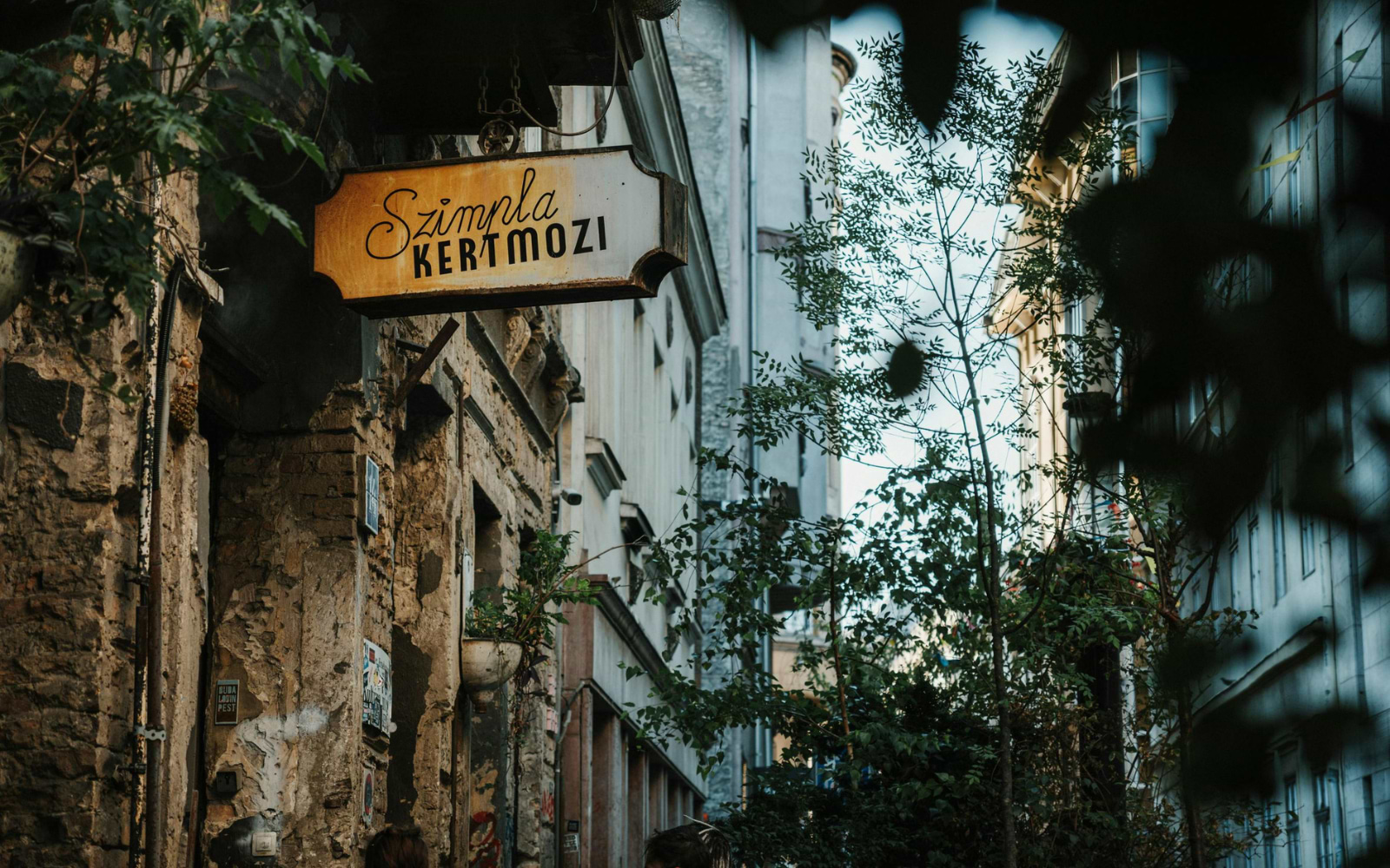 	Yellow hand-lettered Szimpla Kertmozi sign hanging on a weathered building in Budapest's Jewish Quarter