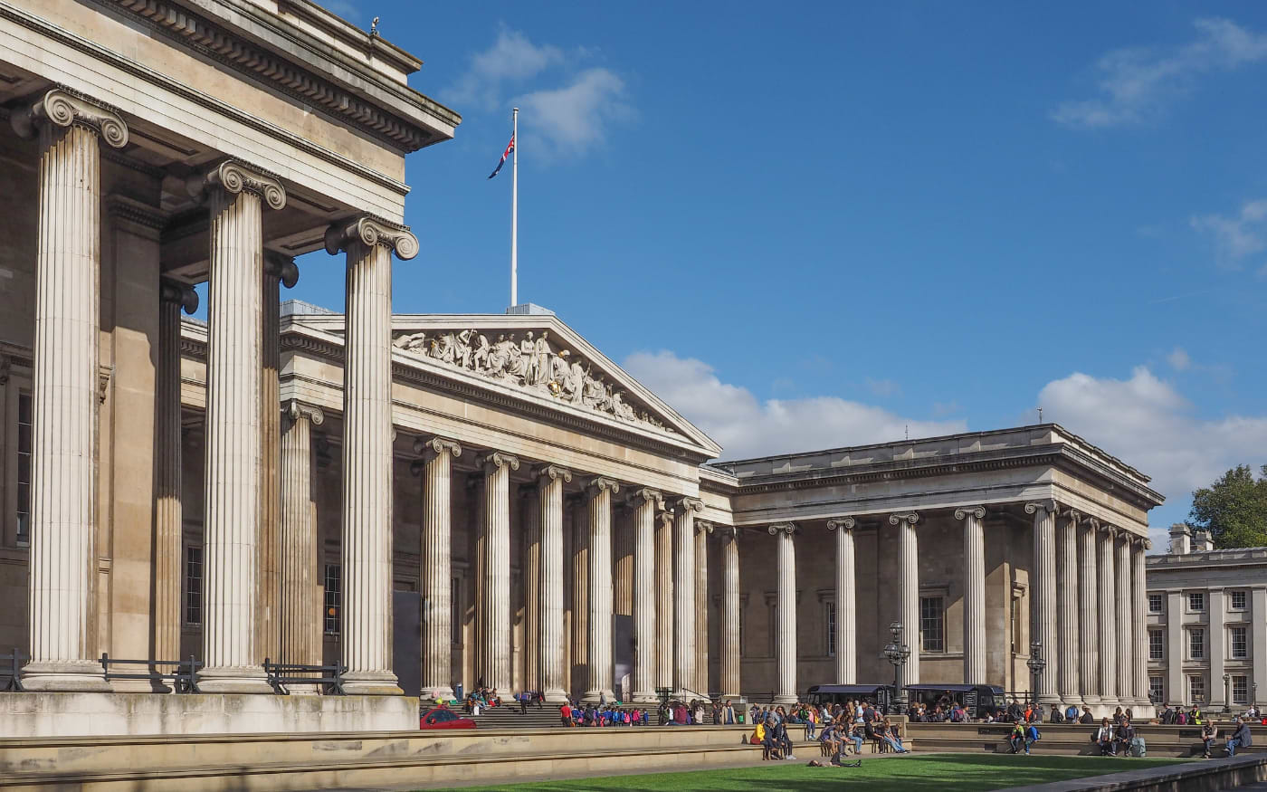 British Museum colonnade with Ionic columns and Union flag, visitors relaxing on the forecourt, a top free museum in London