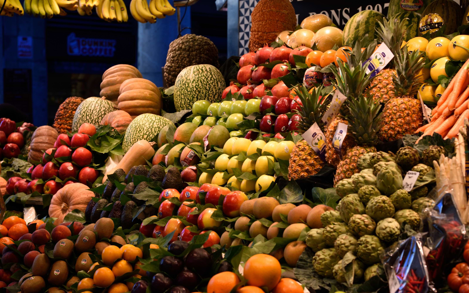 A colourful fruit stall overflowing with pineapples, apples, melons, artichokes and bananas.
