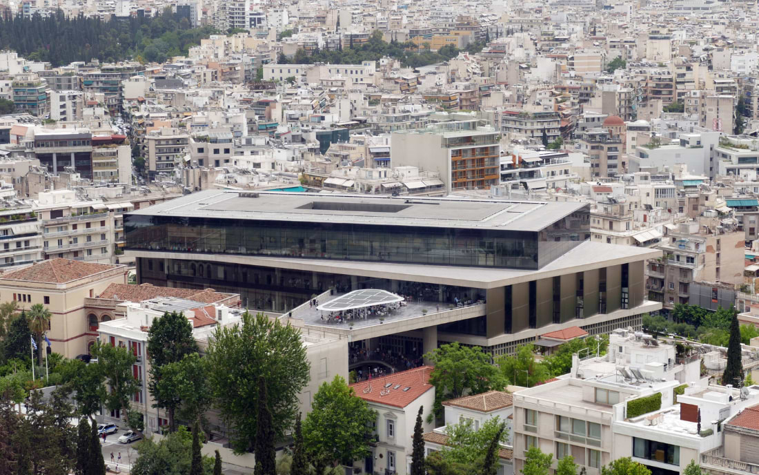 Aerial view of the Acropolis Museum Athens, a modern glass and steel building set within the dense urban cityscape of Athens