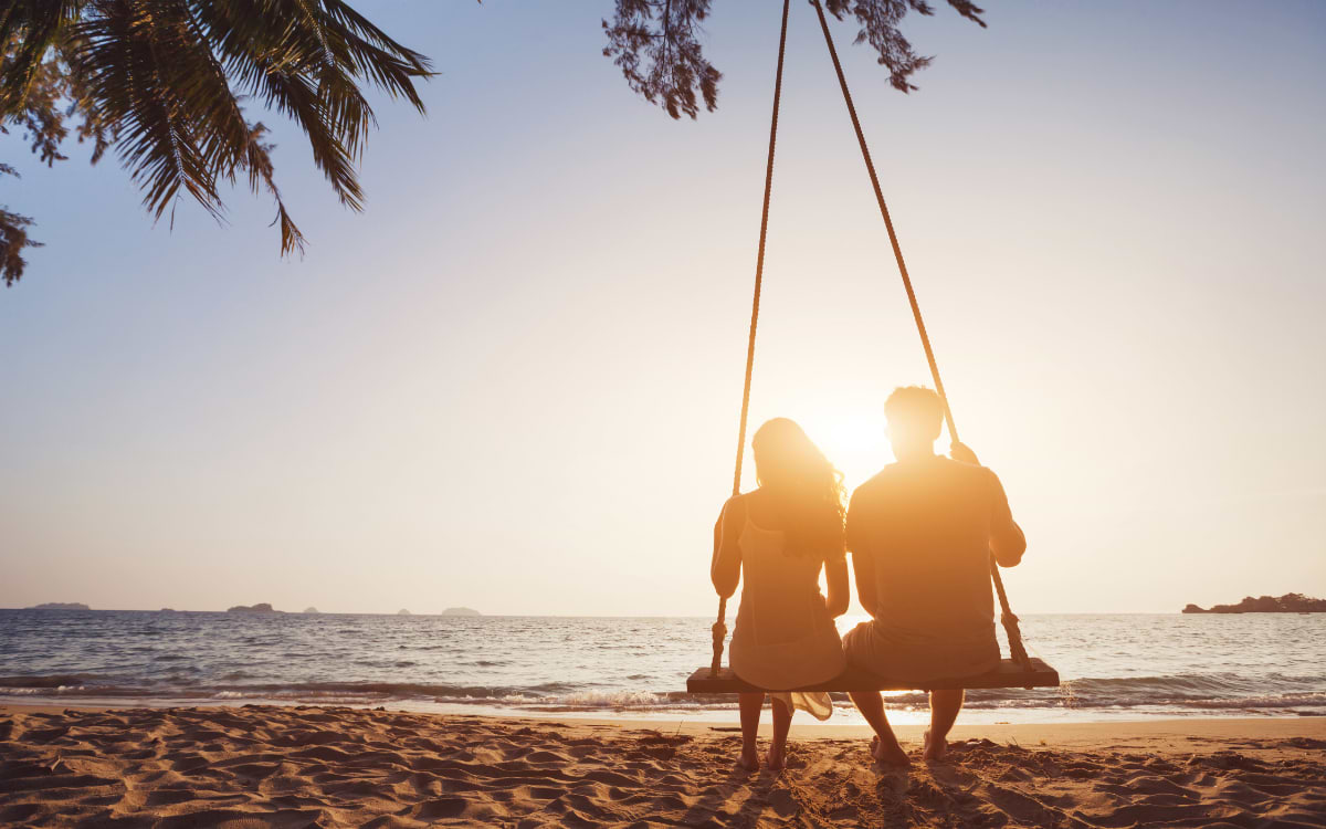 Couple sitting on a beach swing at sunset watching the ocean