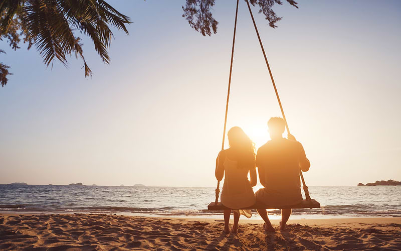 Couple sitting on a beach swing at sunset watching the ocean