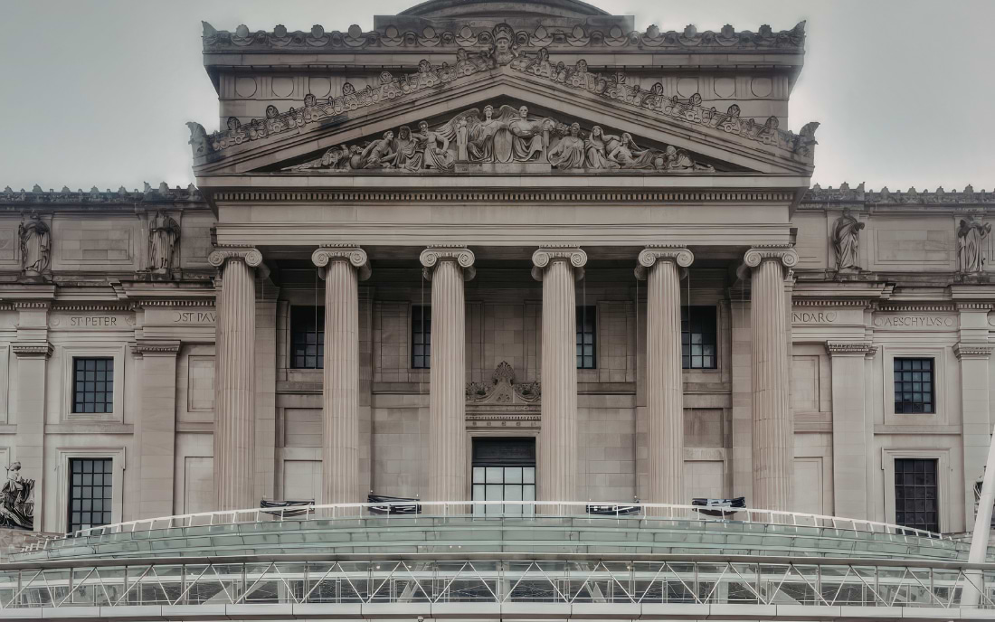 Neoclassical facade of the British Museum in London, with tall Ionic columns, ornate sculptural reliefs on the pediment, and a modern glass canopy at the entrance