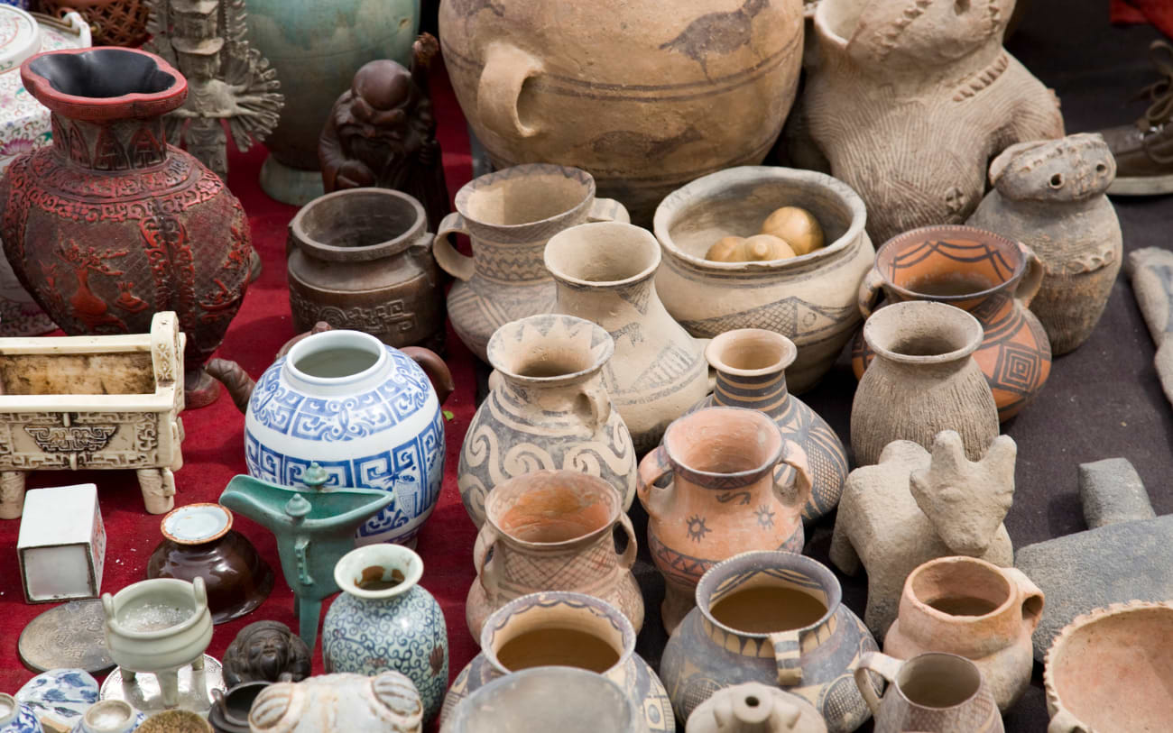 Colourful collection of antique ceramic pots, vases and figurines displayed on a red cloth at an Athens flea market stall