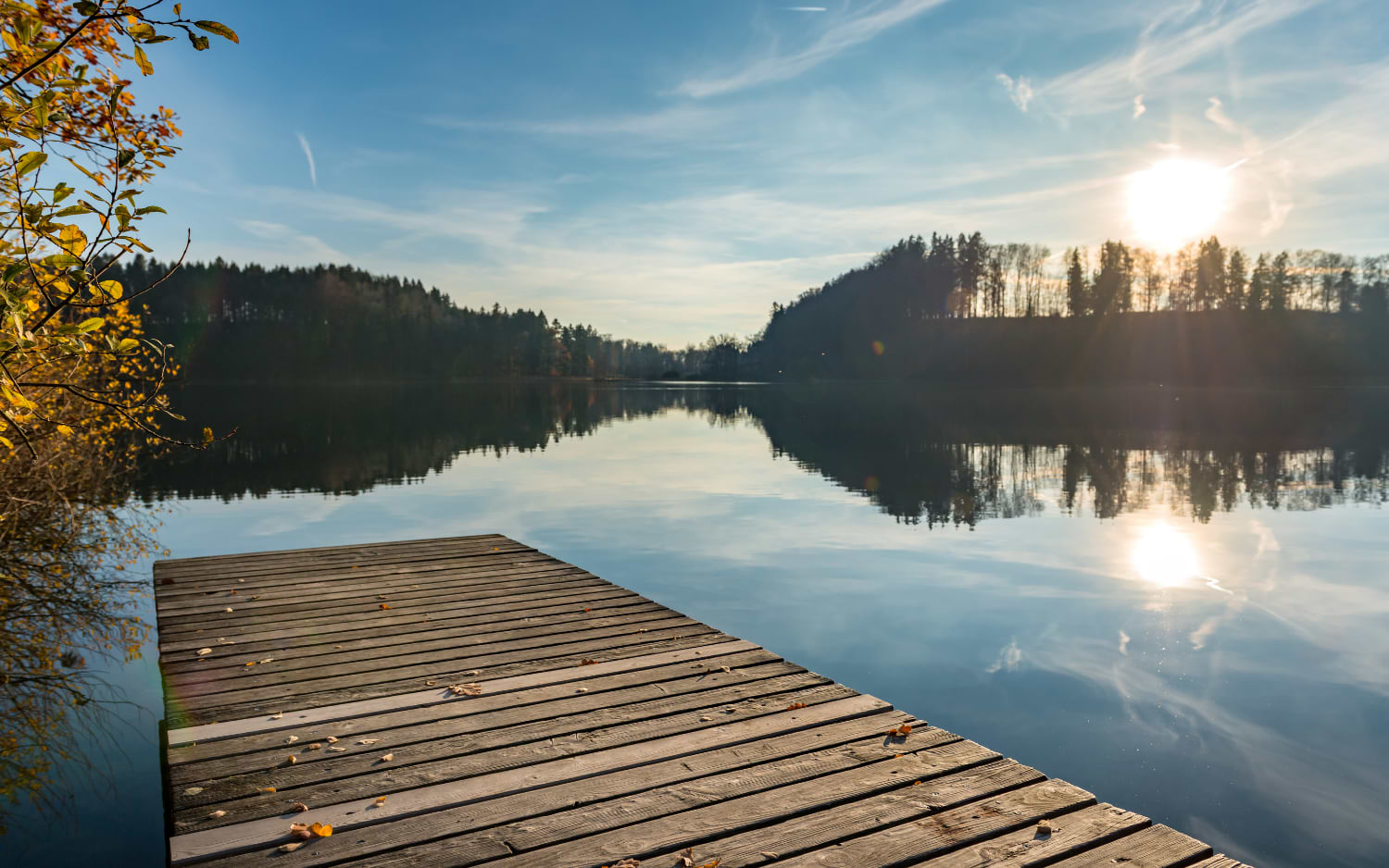 Wooden jetty on a calm autumn lake with golden trees, Türlersee circular walk near Zurich