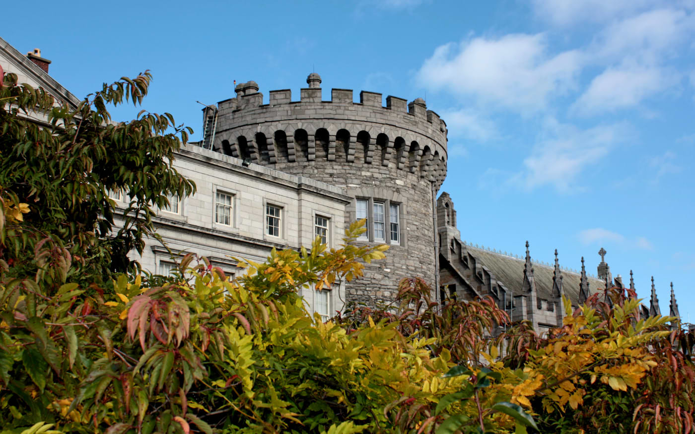 Dublin Castle's round Record Tower and the Gothic Chapel Royal behind yellow and red autumn foliage under a blue sky