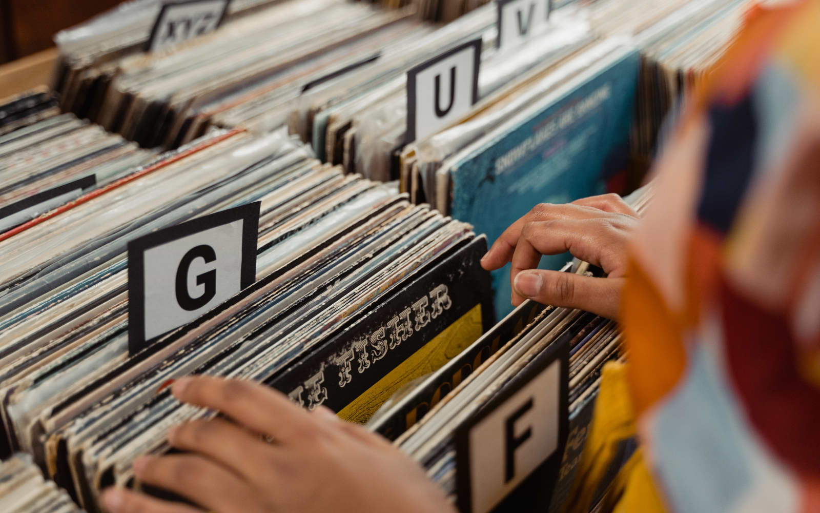 Two people flip through vinyl records in alphabetised crates marked F, G, U and V at a record fair