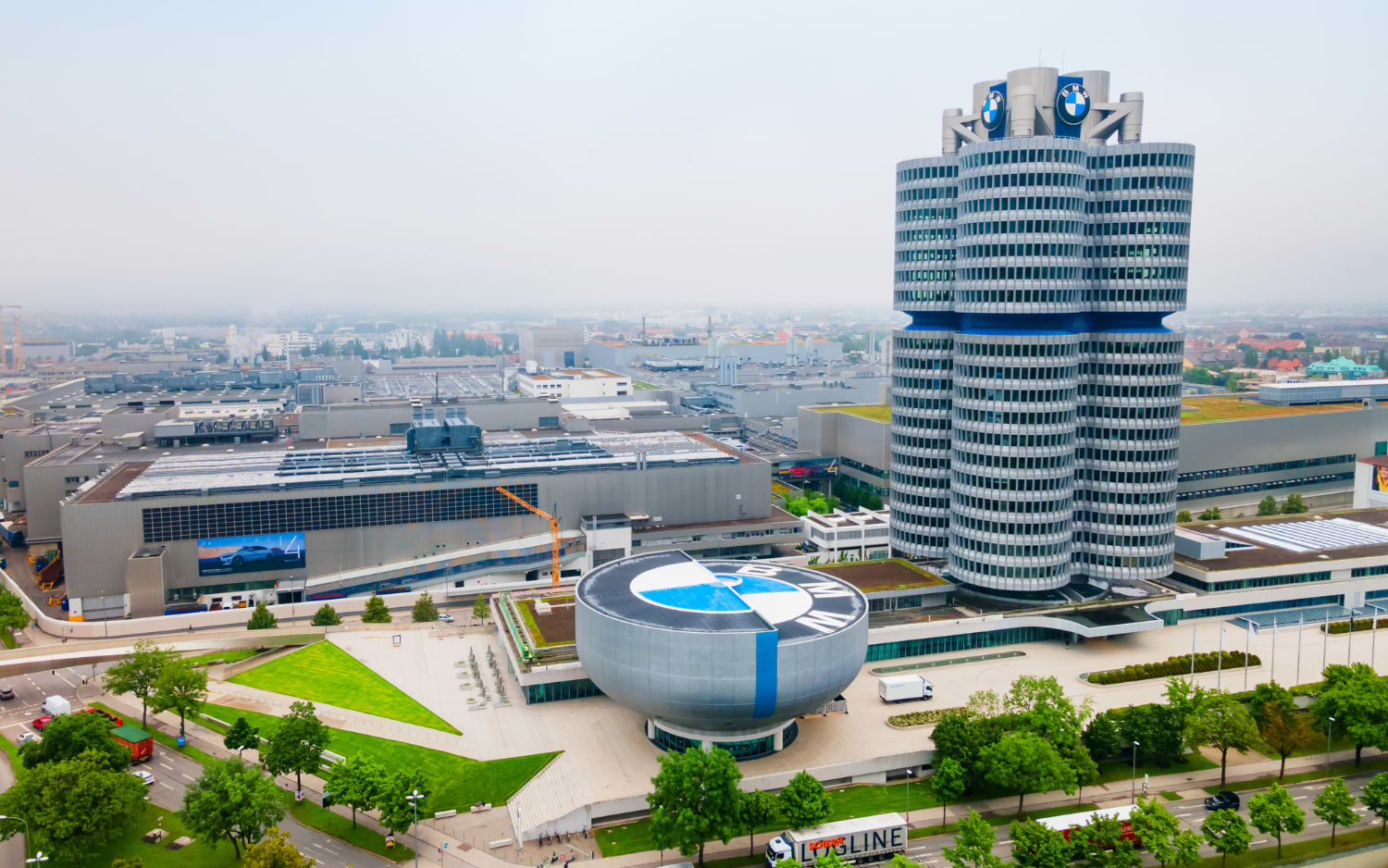 Aerial view of the BMW Museum's silver bowl-shaped building beside the four-cylinder BMW headquarters tower in Munich, Germany.