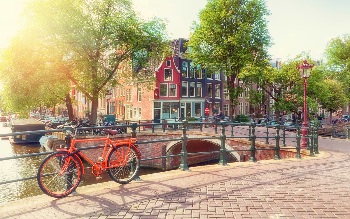 Rotes Fahrrad auf einer Grachtenbrücke im besten Viertel Amsterdam bei Sonnenaufgang