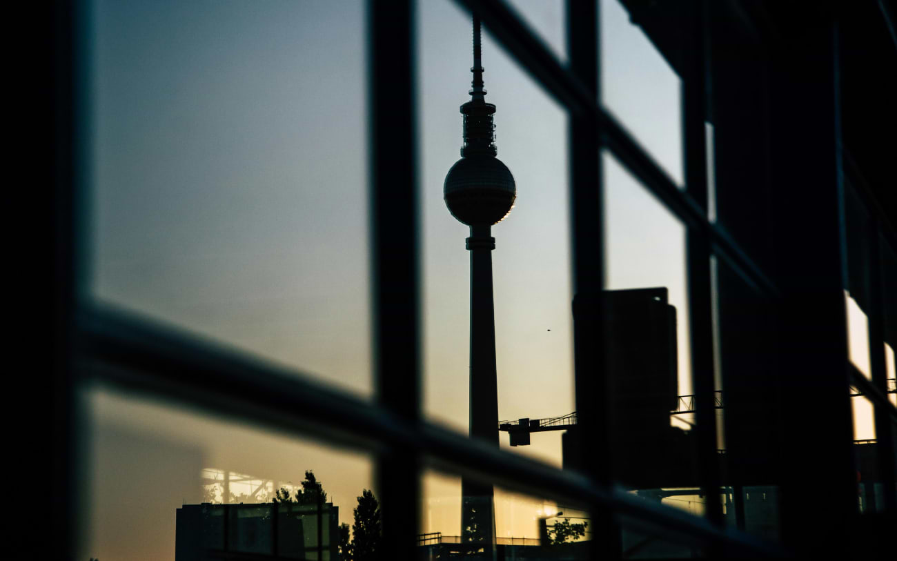 Fernsehturm silhouetted against a golden dusk sky, seen through the glass panels of a rooftop bar in Berlin