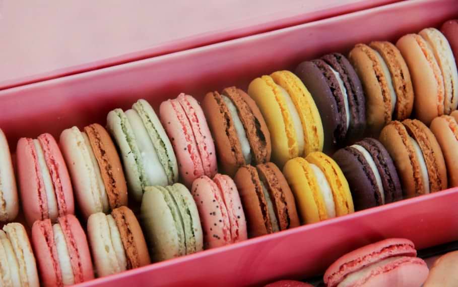 A close-up of a tray filled with colorful macarons in various flavors at a Parisian patisserie