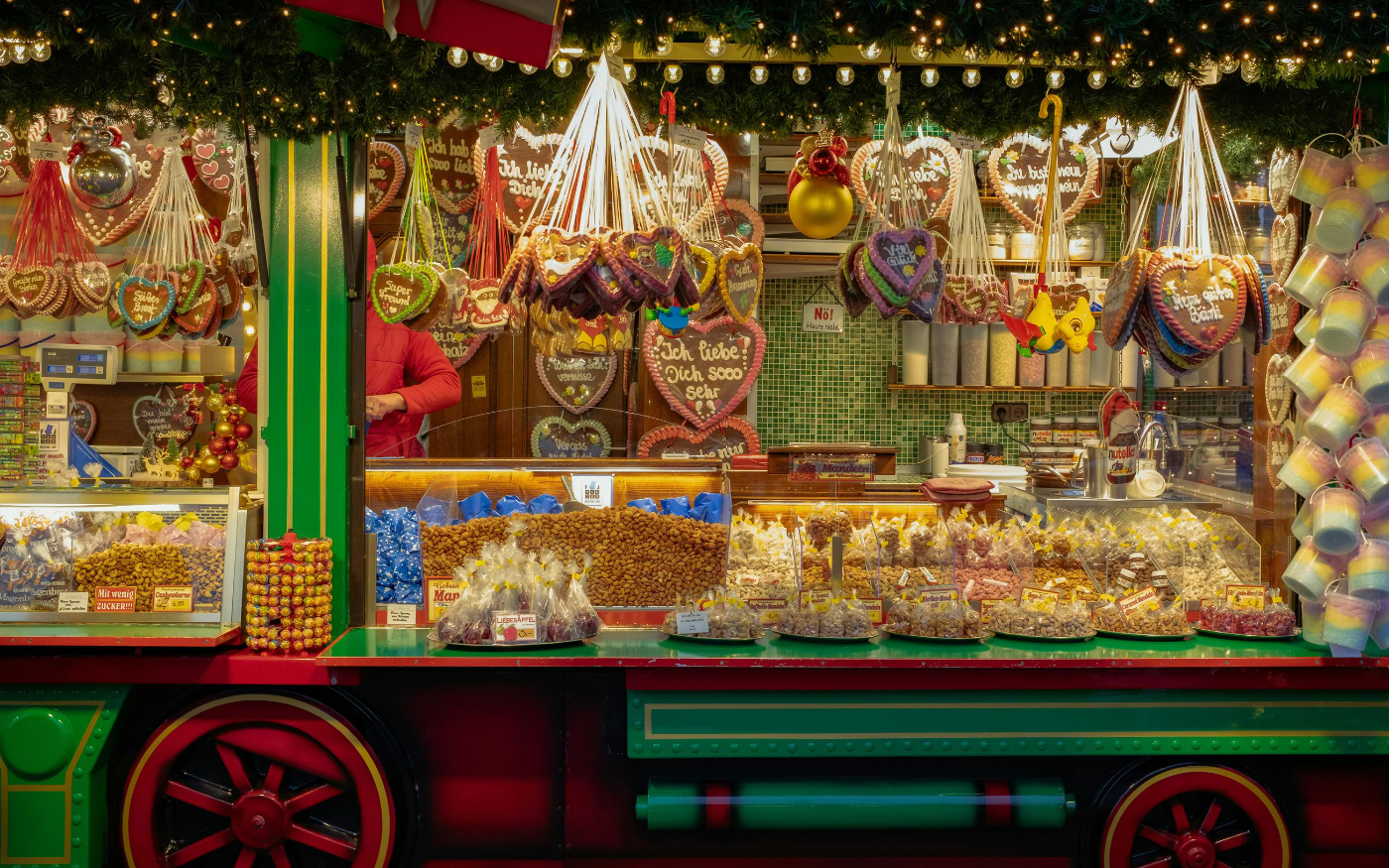 Christmas market stall with gingerbread hearts, roasted almonds and sweets in a red and green train-shaped booth