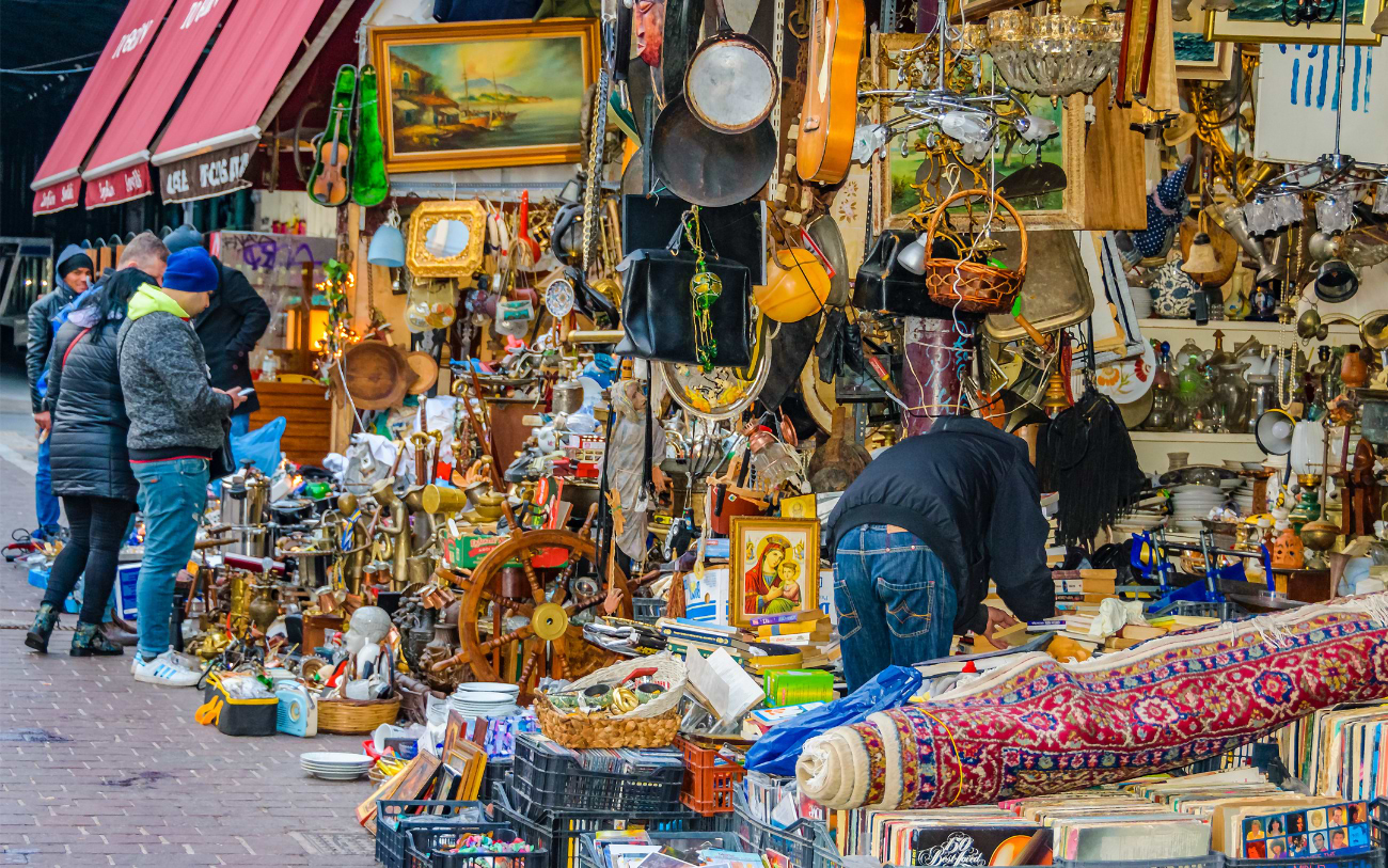 Crowded flea market stall in Athens overflowing with antiques, paintings, brass items, rugs and second-hand goods