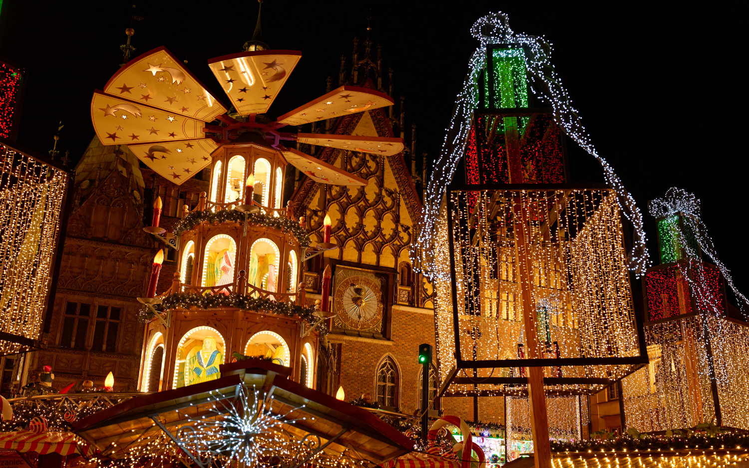 Illuminated wooden Christmas pyramid and giant light-up gift boxes in front of a Gothic town hall at night