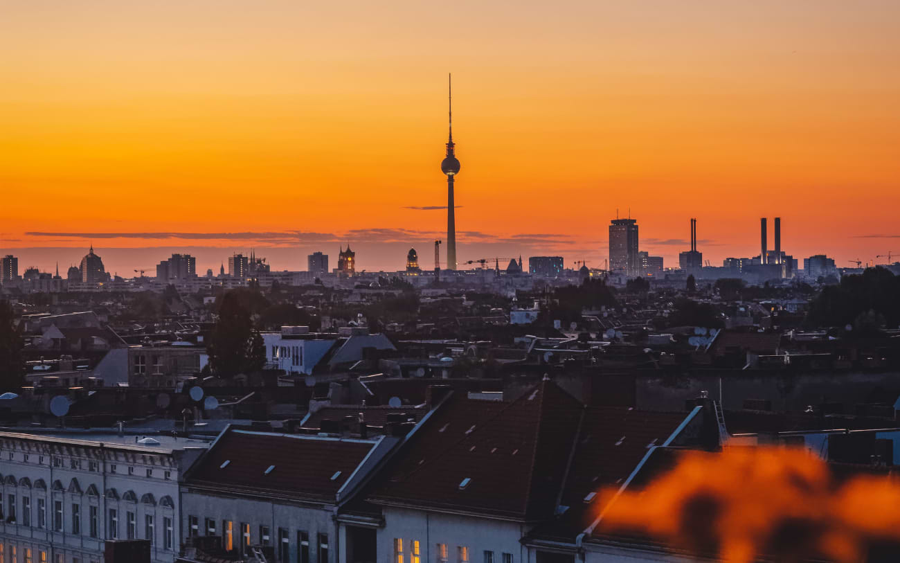 Berlin skyline at sunset from a rooftop in Neukölln, Fernsehturm against a vivid orange sky above red rooftops