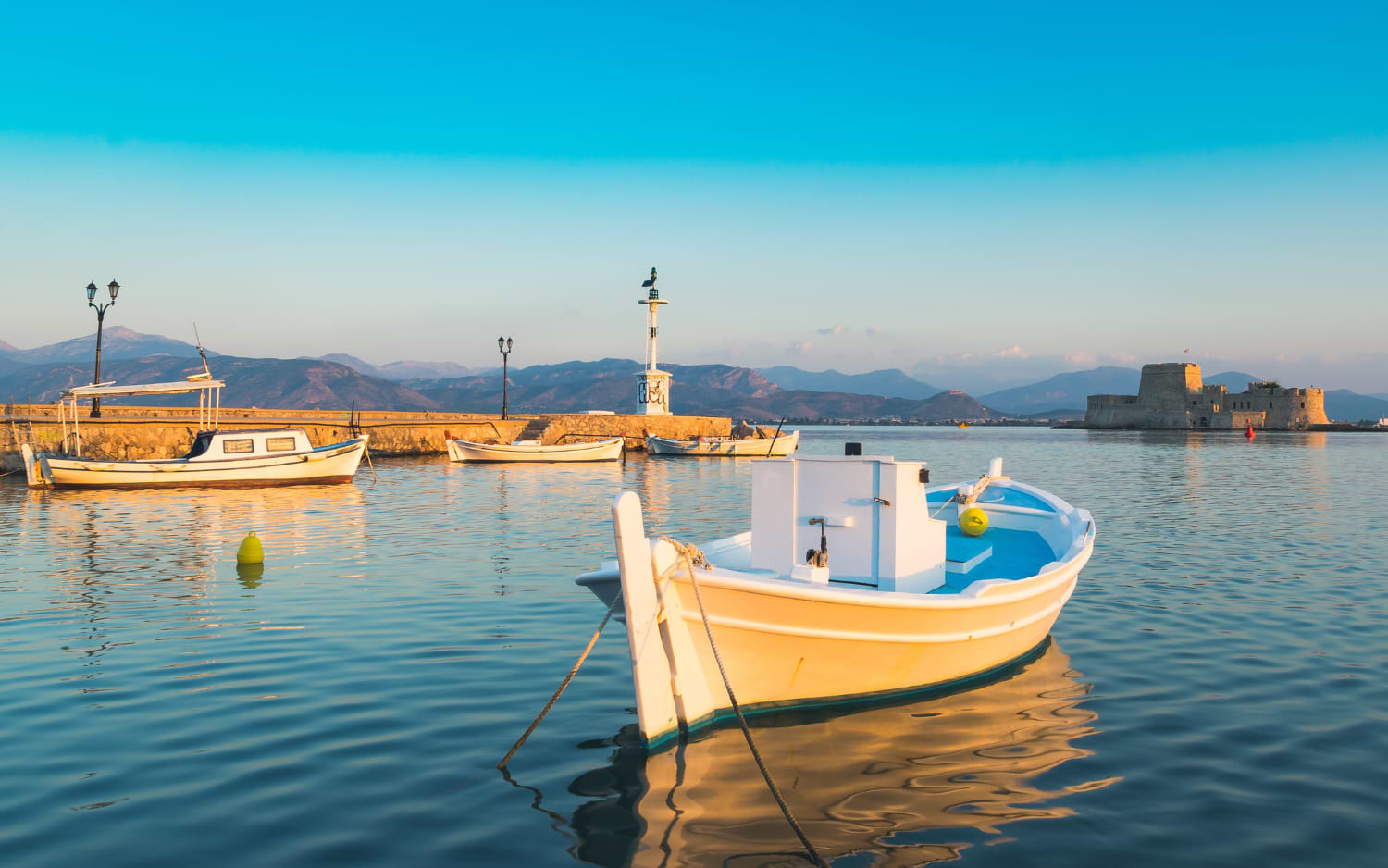 Traditional white fishing boats at Nafplio harbour at golden hour, Bourtzi fortress island in background