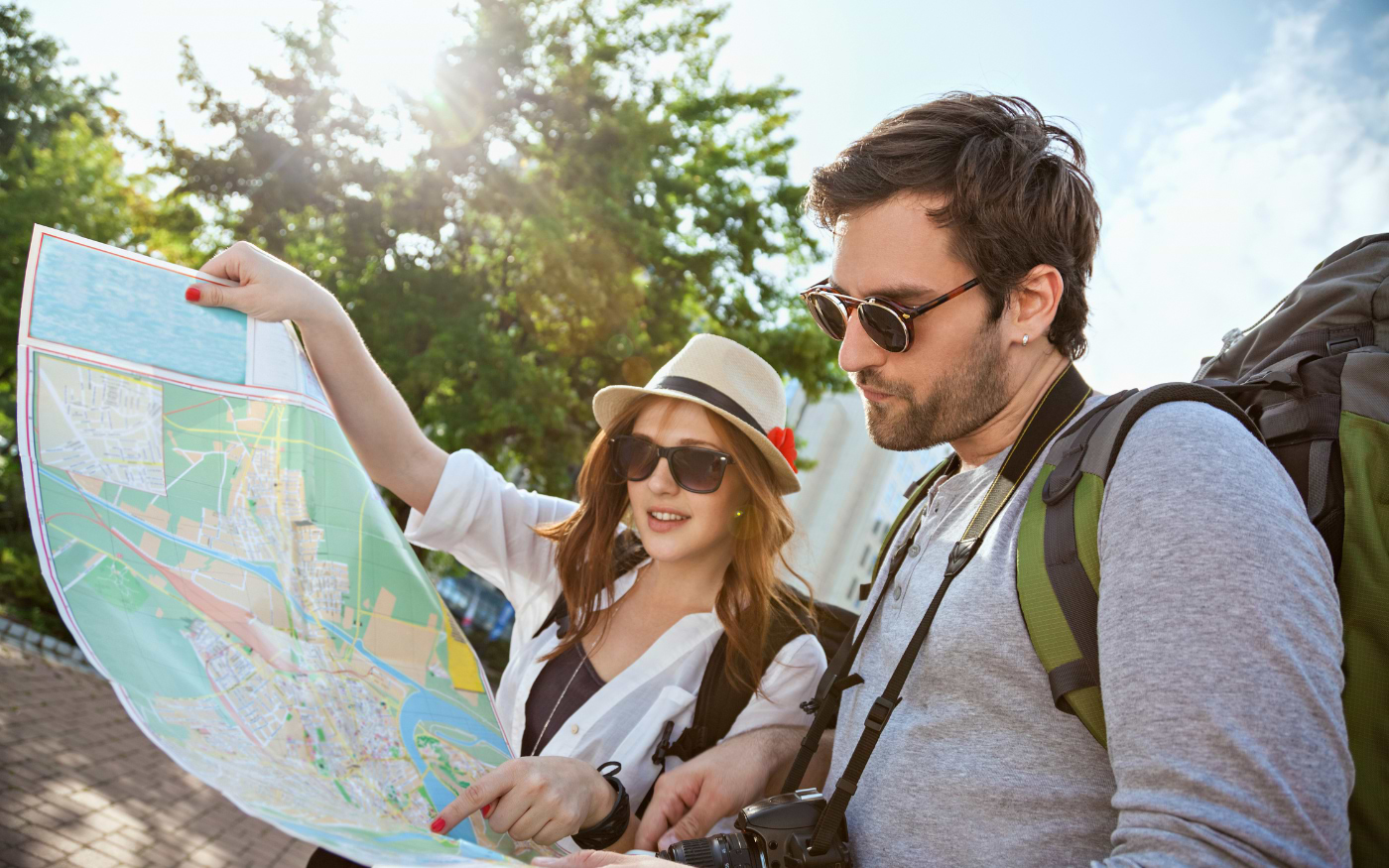 Young couple with backpacks and camera reading a city map outdoors on a sunny short city break