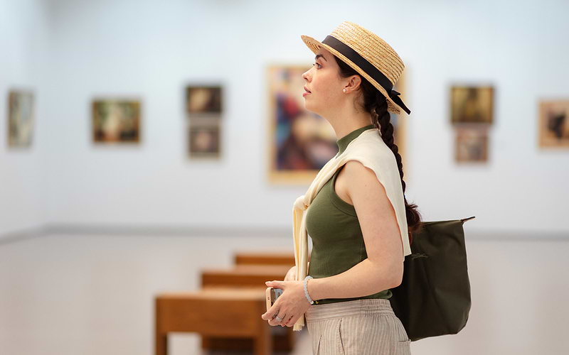 Woman in a straw boater hat viewing paintings in a bright art gallery, a typical moment in Vienna museums