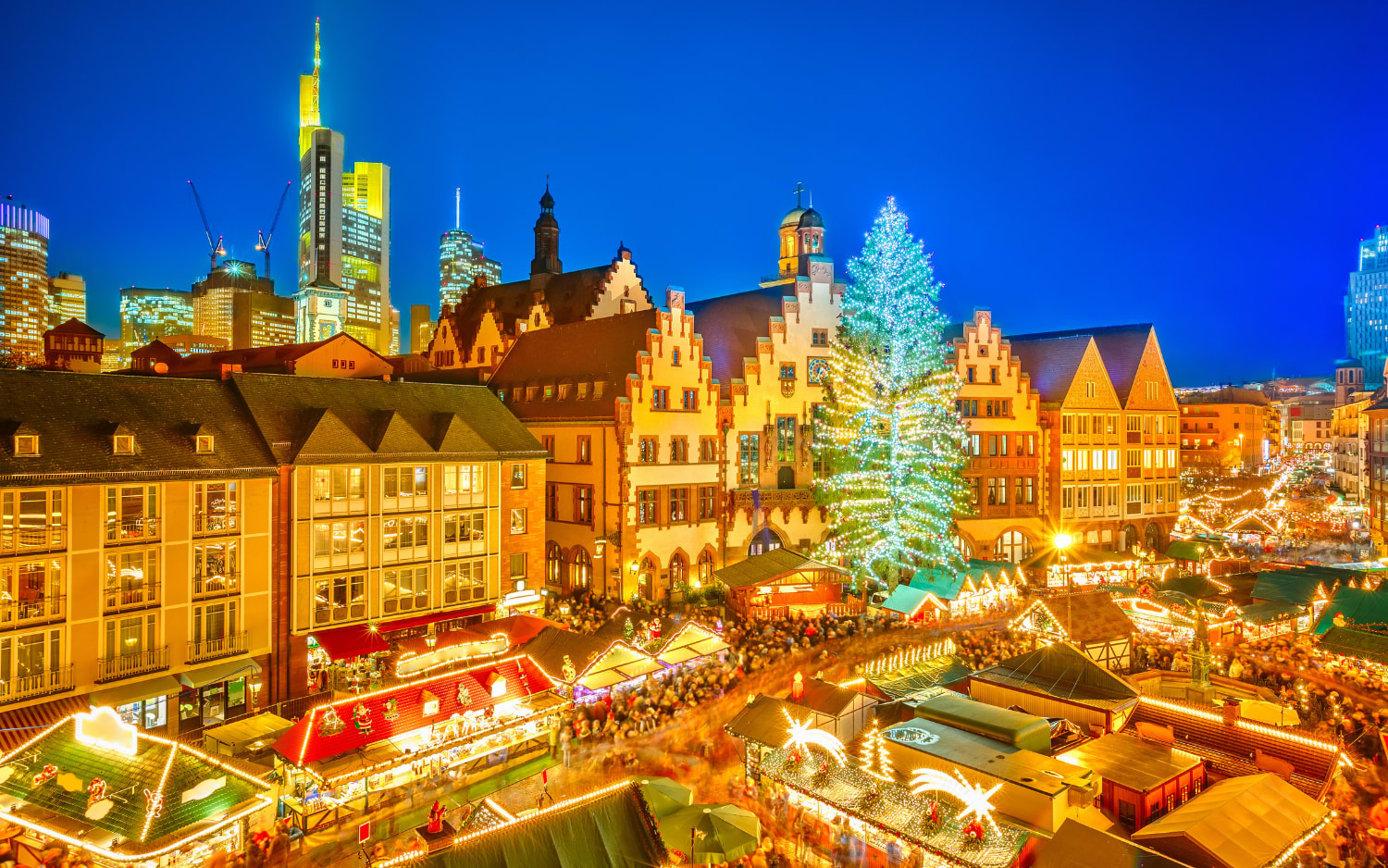 Frankfurt Christmas market on Rƶmerberg at dusk, with a lit tree, half-timbered houses and the city skyline behind