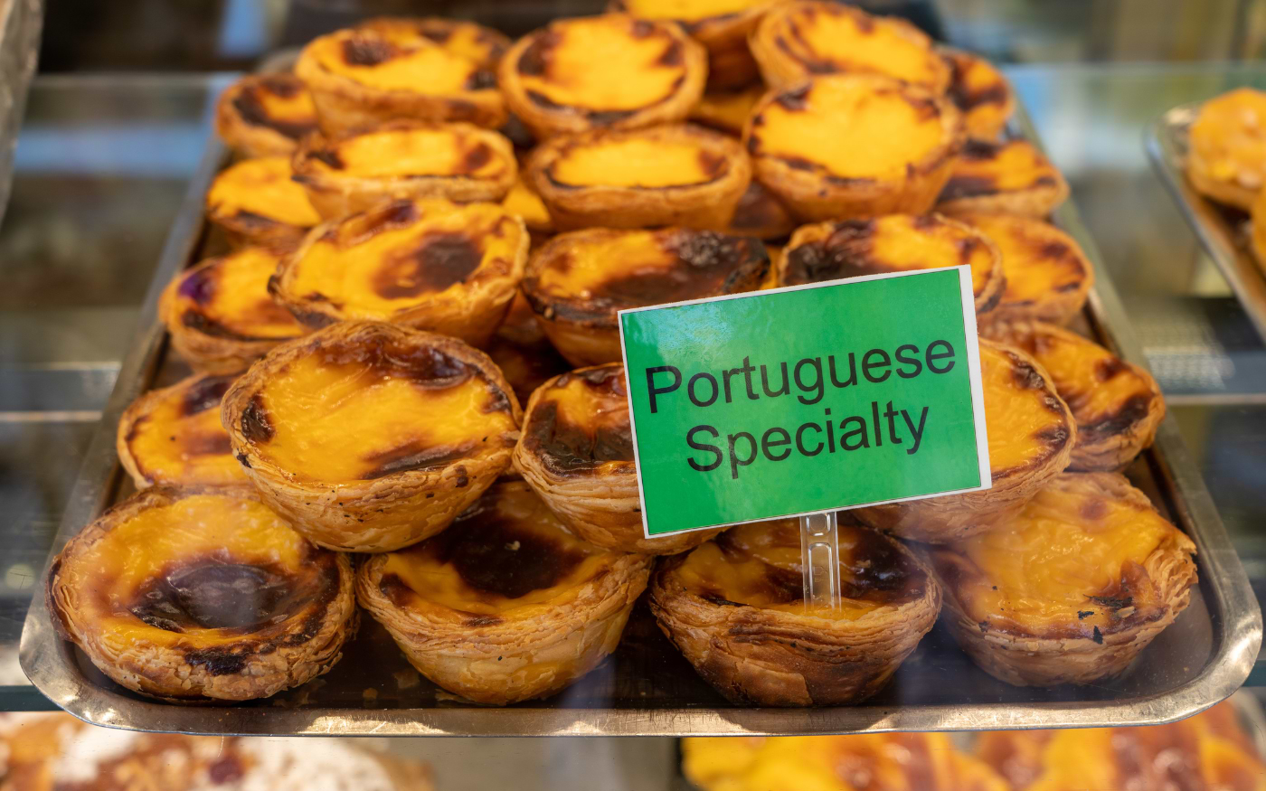 Freshly baked pastƩis de nata, traditional Portuguese custard tarts, displayed in a bakery showcase window.