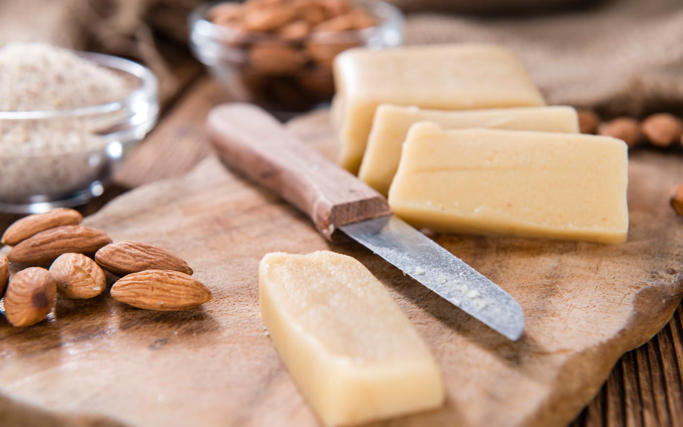 Sliced marzipan bars on a wooden board with whole almonds and a knife