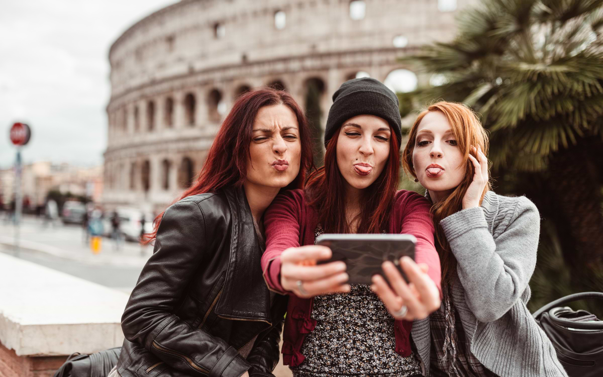 Three women pulling funny faces while taking a selfie in front of the Colosseum in Rome, hen do city break
