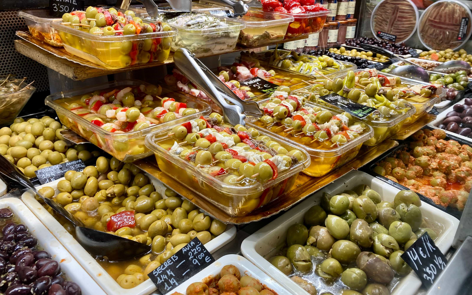 Trays of marinated olives, pintxos and stuffed peppers on display at a Barcelona market stall.