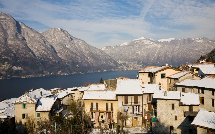 The serene winter landscape of Lake Como, with snow-capped mountains reflecting on the calm waters and quaint lakeside villages