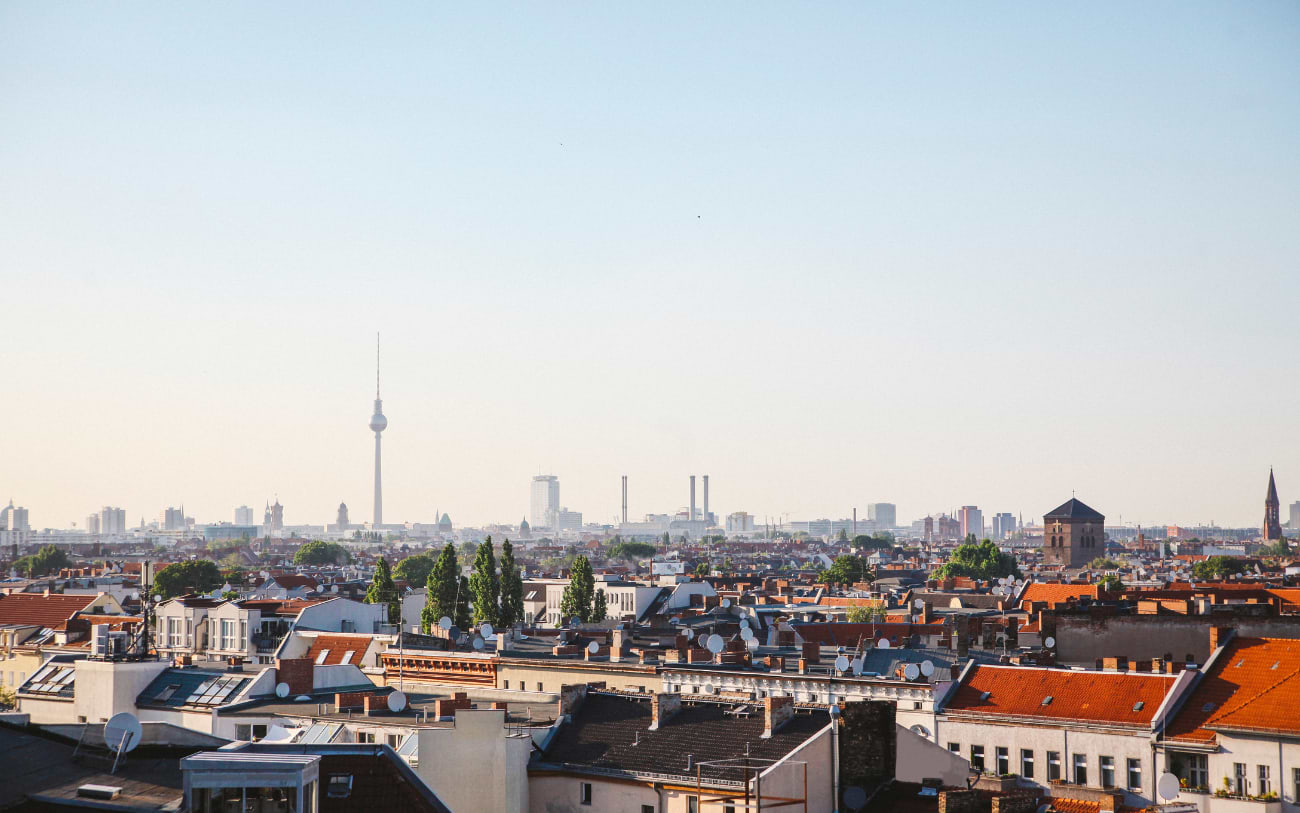Panoramic rooftop view over Berlin red-tiled residential rooftops with the Fernsehturm visible in the hazy distance