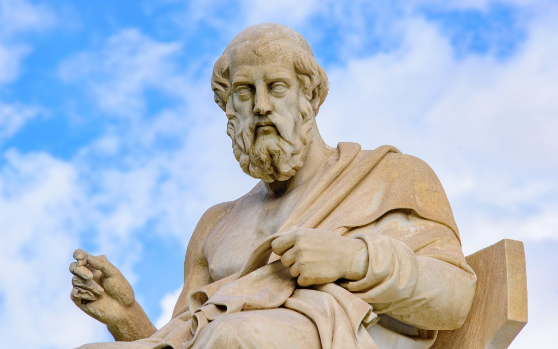 Close-up of a marble statue of Plato seated with one hand raised, against a blue sky with white clouds, at the Academy of Athens