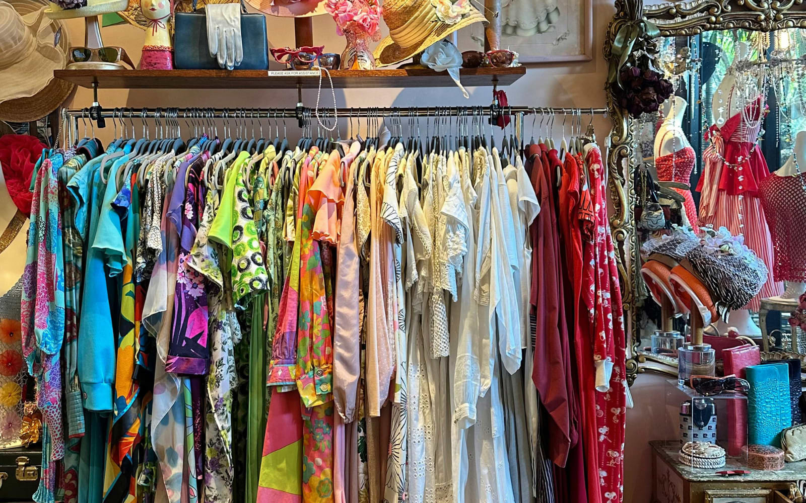 Rack of colourful vintage dresses below a shelf of hats, gloves and bags in a Budapest vintage shop