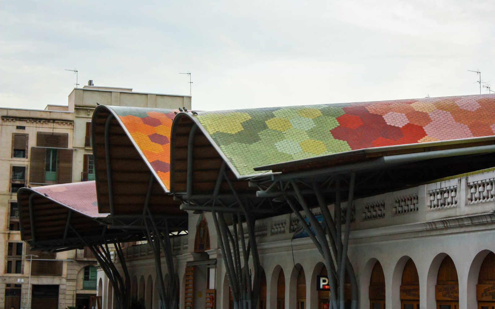 Wavy mosaic-tiled roof of Mercat de Santa Caterina glowing orange, green and red against a cloudy Barcelona sky.