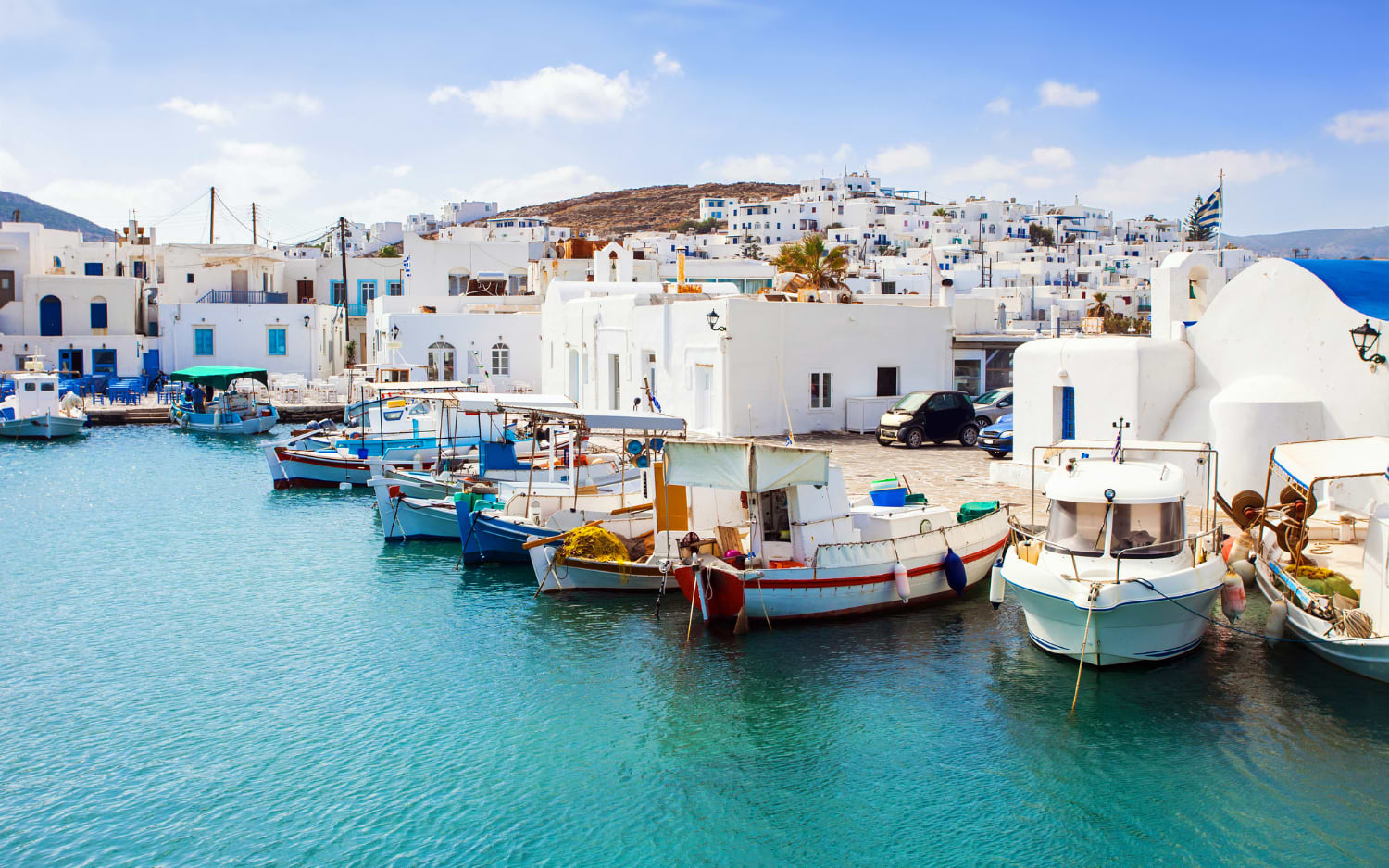 Fishing boats moored at Naoussa harbour, Paros, with whitewashed Cycladic buildings climbing the hillside