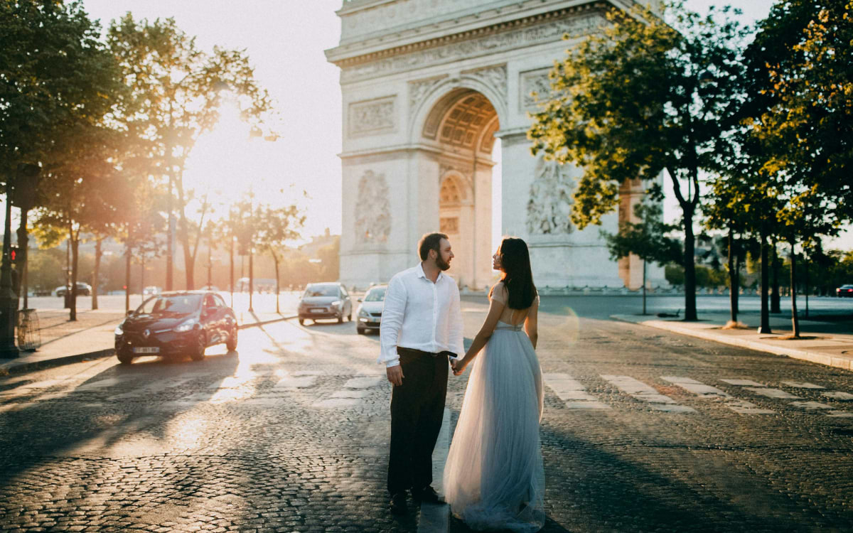 Couple in wedding attire holding hands near Arc de Triomphe, Paris