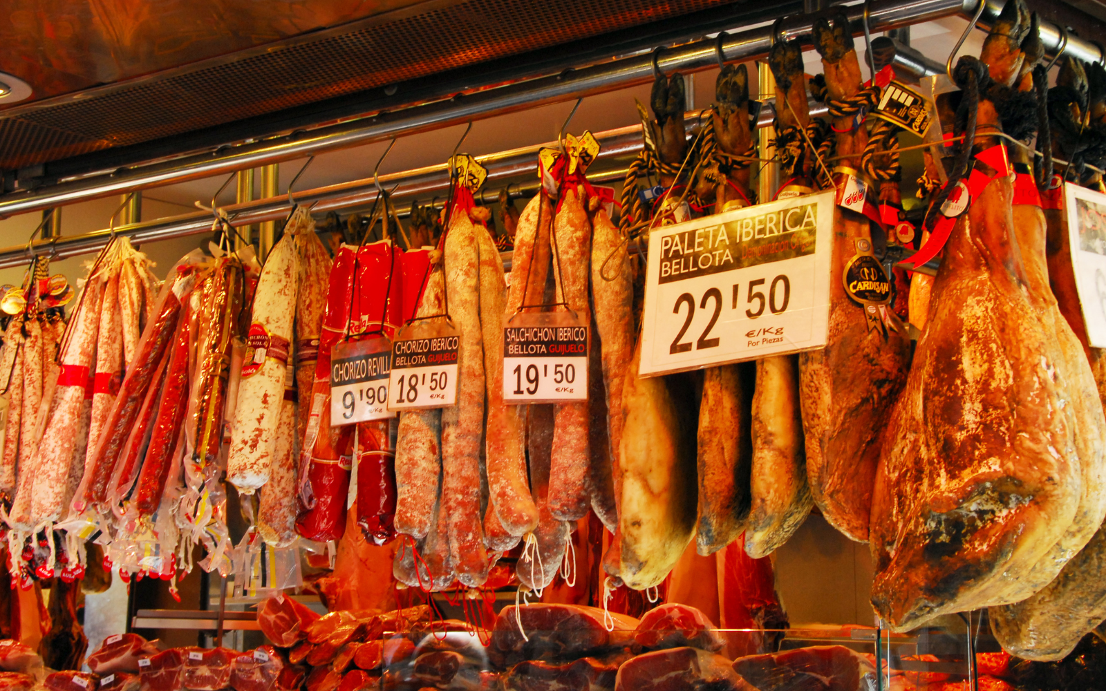 Cured Iberian hams, chorizo and salchichón hang with price tags at a Barcelona market meat stall.