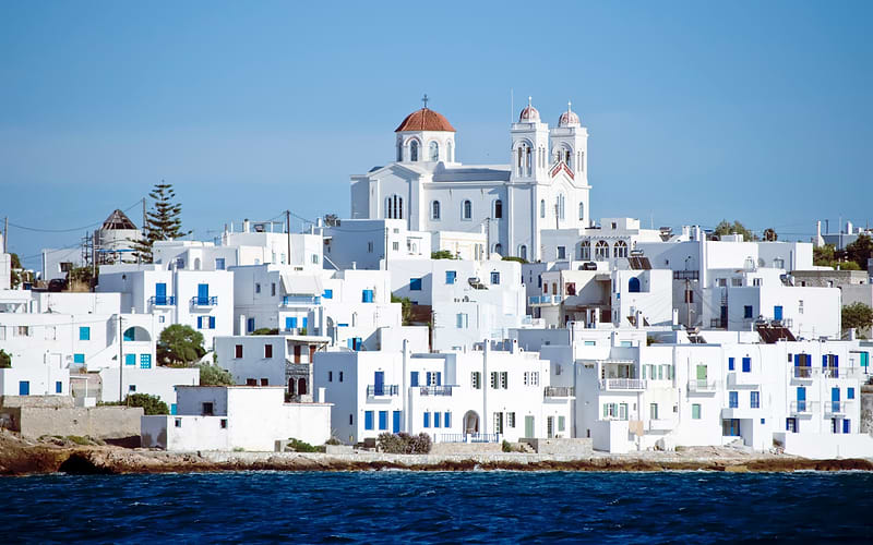 Whitewashed Cycladic village of Naoussa on Paros seen from the sea, church with red domes crowning the hill